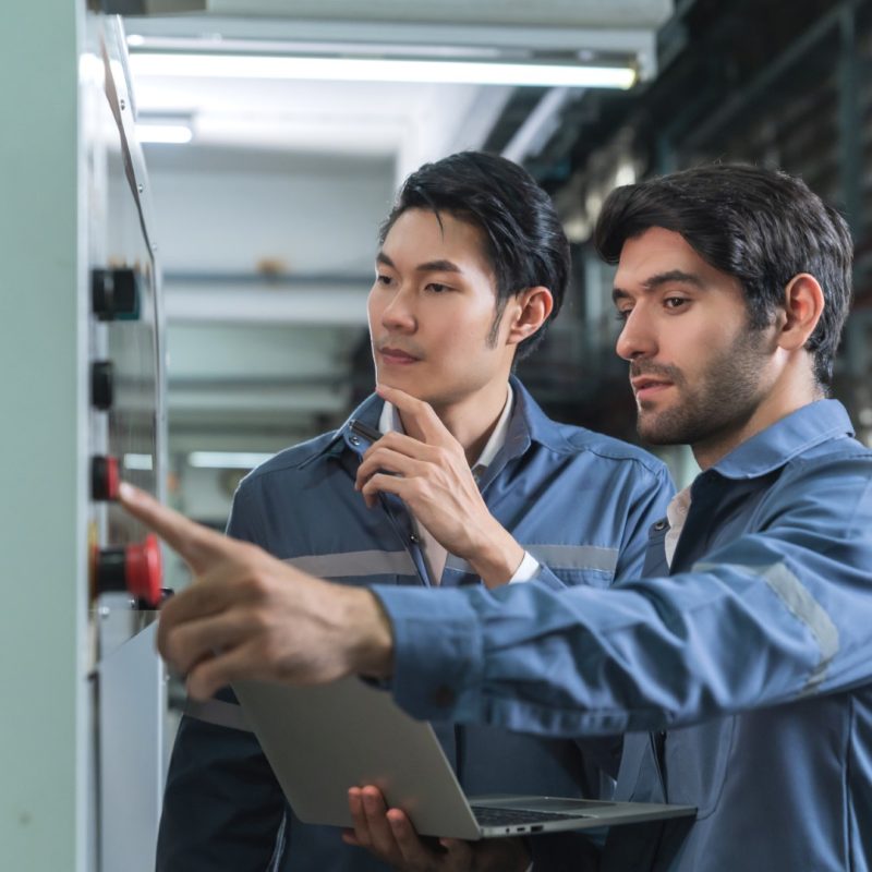 Male Asian caucasian engineer professional having a discussion standing consult at machine in the factory ,two expert coworker brainstorm explaining and solves the process of the cnc operate machine